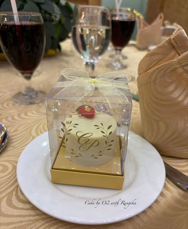 White wedding favour mini cake with a gold monogram and leaf wreath, topped with a strawberry, in a clear gift box