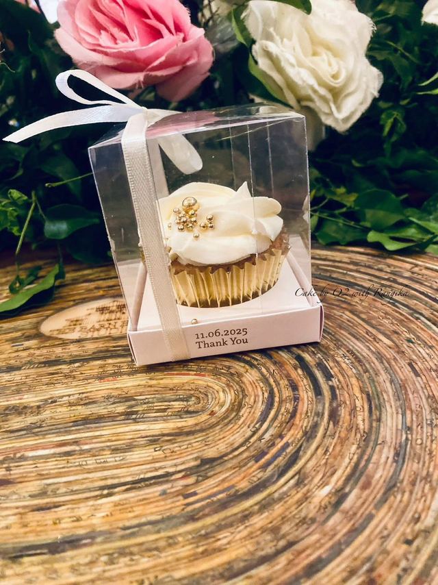 Vanilla wedding favour cupcake with swirled buttercream and gold pearls in a clear thank-you gift box, with roses behind