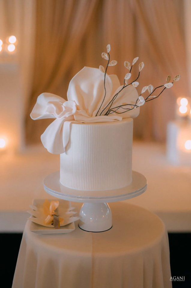 Single-tier ivory cake with fondant bow and gilded leaf branches