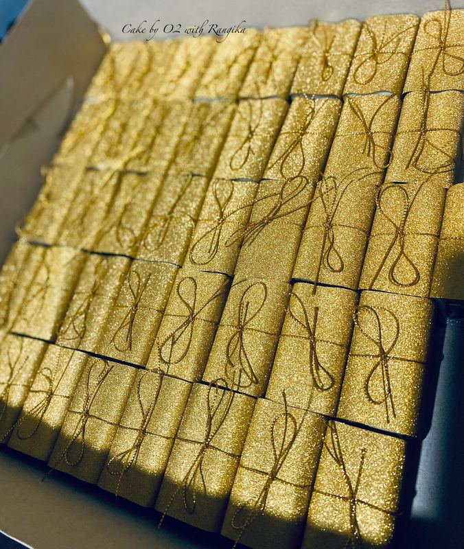 A boxful of mini wedding favour cakes individually wrapped in shimmering gold paper, each tied with a fine gold cord bow, by Cake by O2 in Colombo