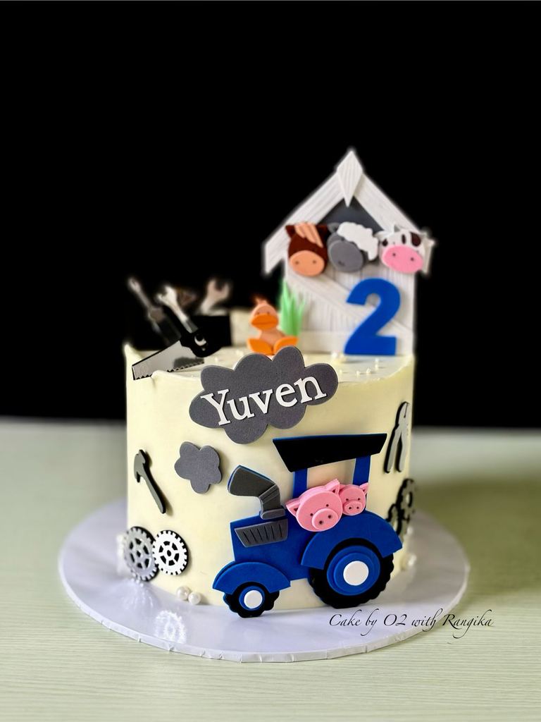 Farm-themed second birthday cake with a blue fondant tractor, pigs, barn animals, tools and the name Yuven, by Cake by O2