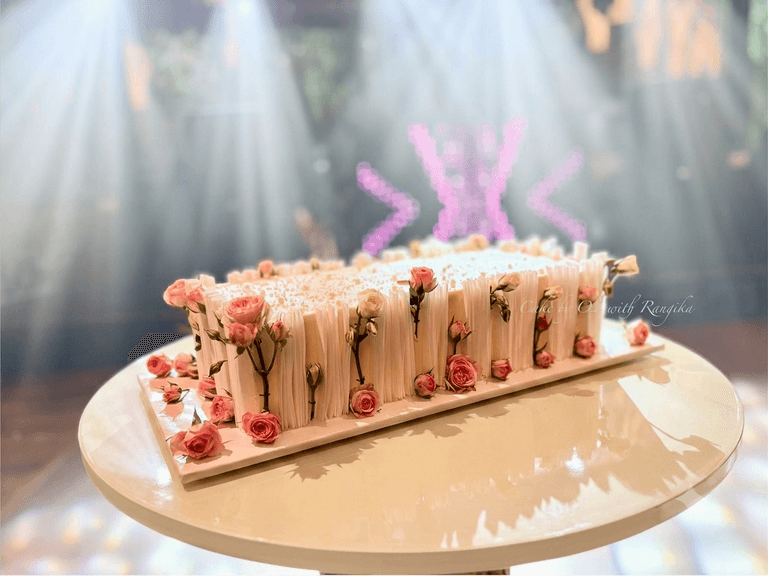 Long white chocolate slab wedding cake covered in vertical white chocolate planks and decorated with pink roses, on a white plinth, by Cake by O2 in Colombo