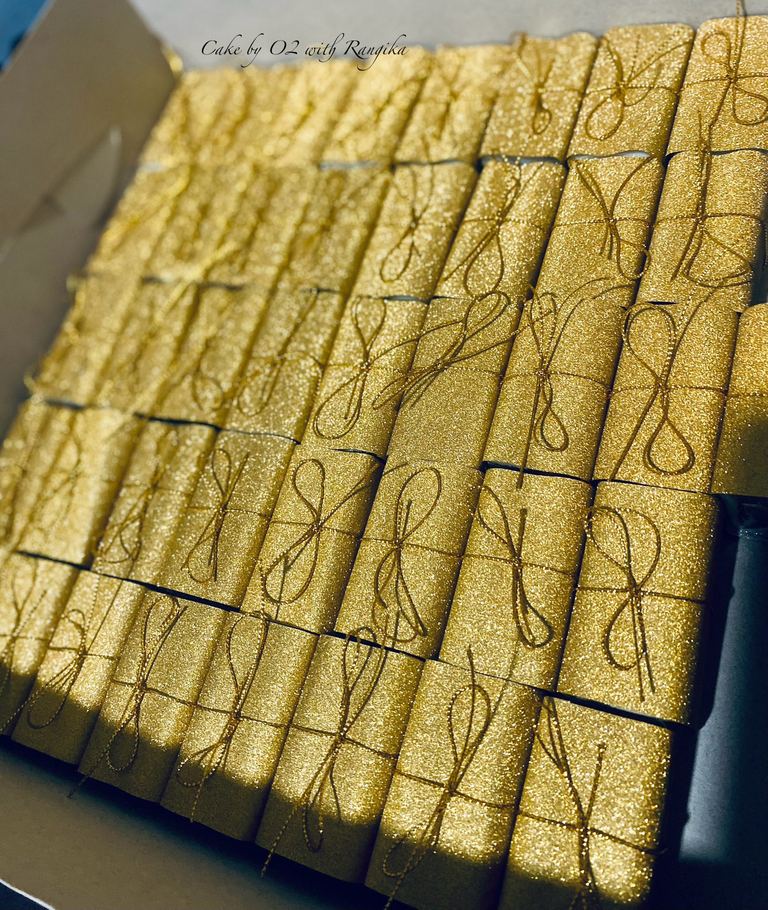 A boxful of mini wedding favour cakes individually wrapped in shimmering gold paper, each tied with a fine gold cord bow, by Cake by O2 in Colombo